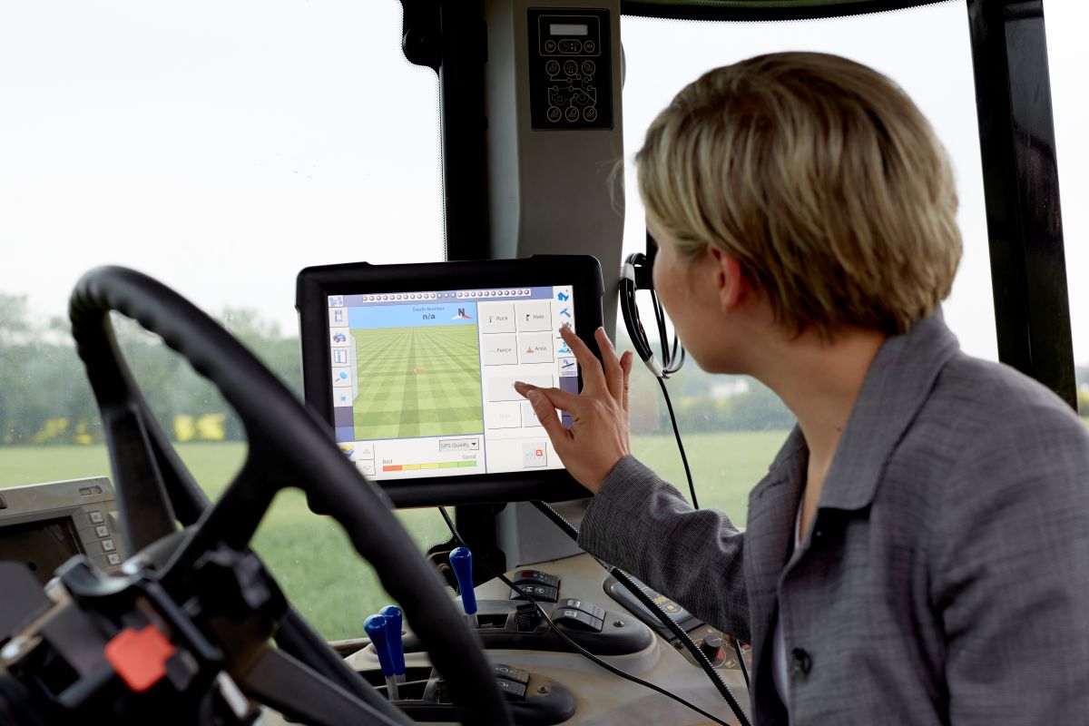 A woman driving a tractor. She is typing on a screen in the cab of the tractor.